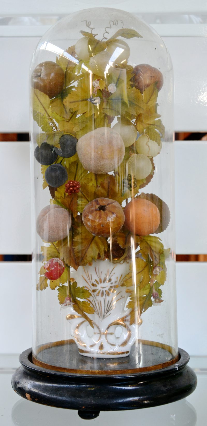 Een glazen stolpje met eronder geblazen glazen vruchtjes en bloemblaadjes.