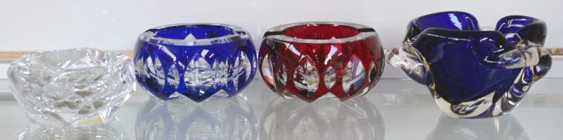 Drie kristallen asbakken van resp. blauw, rood en kleurloos geslepen kristal, gemerkt van Val St. Lambert. We voegen er een geblazen Italiaanse asbak aan toe.