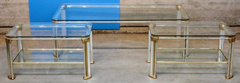 Een grote en twee kleine metalen salontafels met glazen bladen.