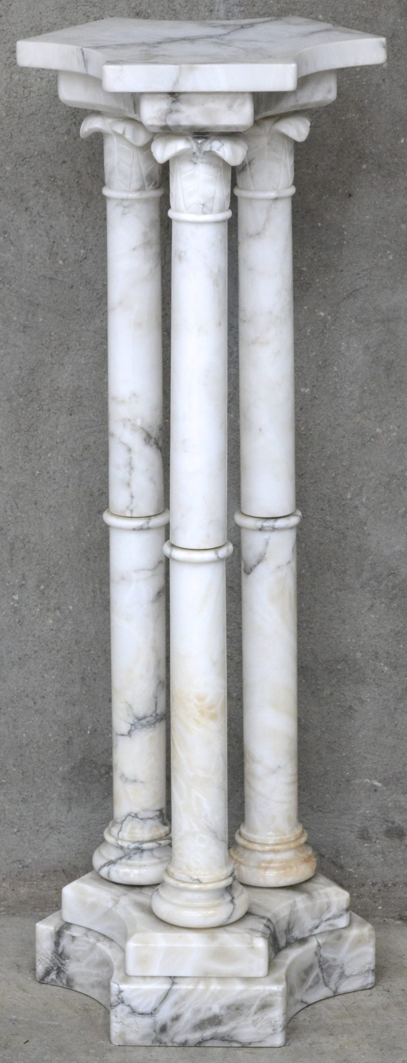 Een marmeren piëdestal in de vorm van drie semi-antieke zuiltjes.