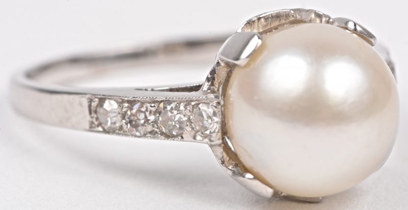 Een 18 karaats wit gouden ring bezet met briljanten met een gezamenlijk gewicht van ± 0,30 ct. en een parel.