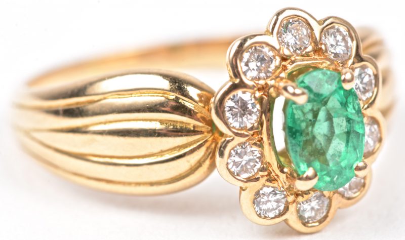 Een 18 karaats geel gouden ring bezet met briljanten met een gezamenlijk gewicht van ± 0,30 ct. en een centrale smaragd van ± 0,50 ct.