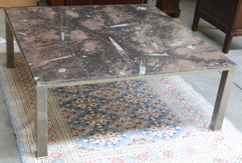 Een grote vierkante salontafel met verchroomde poten en met een marmeren blad (fossiele zeebodem). Modern.