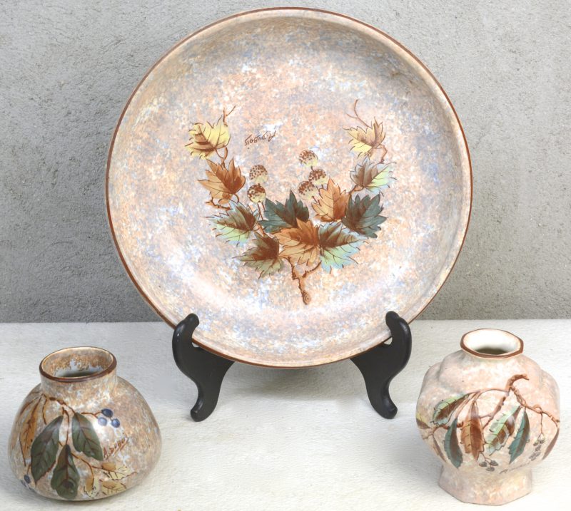 Een schaal en twee vaasjes van meerkleurig aardewerk met een decor van bladeren. Gesigneerd ‘A.Dubois’. Onderaan gemerkt.