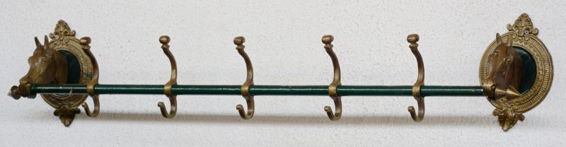 Een metalen kapstok met vijf haken en twee bronzen paardenkoppen als bevestigingspunten.