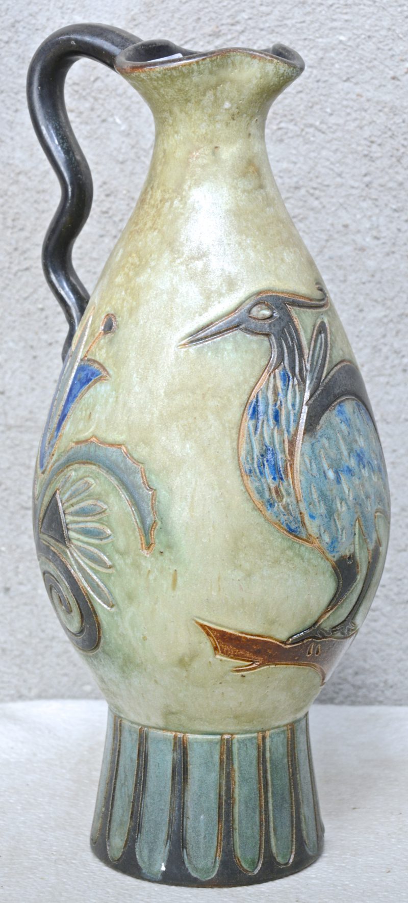 Een art deco vaas van meerkleurig geglazuurd steengoed met een gestileerde vogel en bloemen in het decor. Onderaan gemerkt.