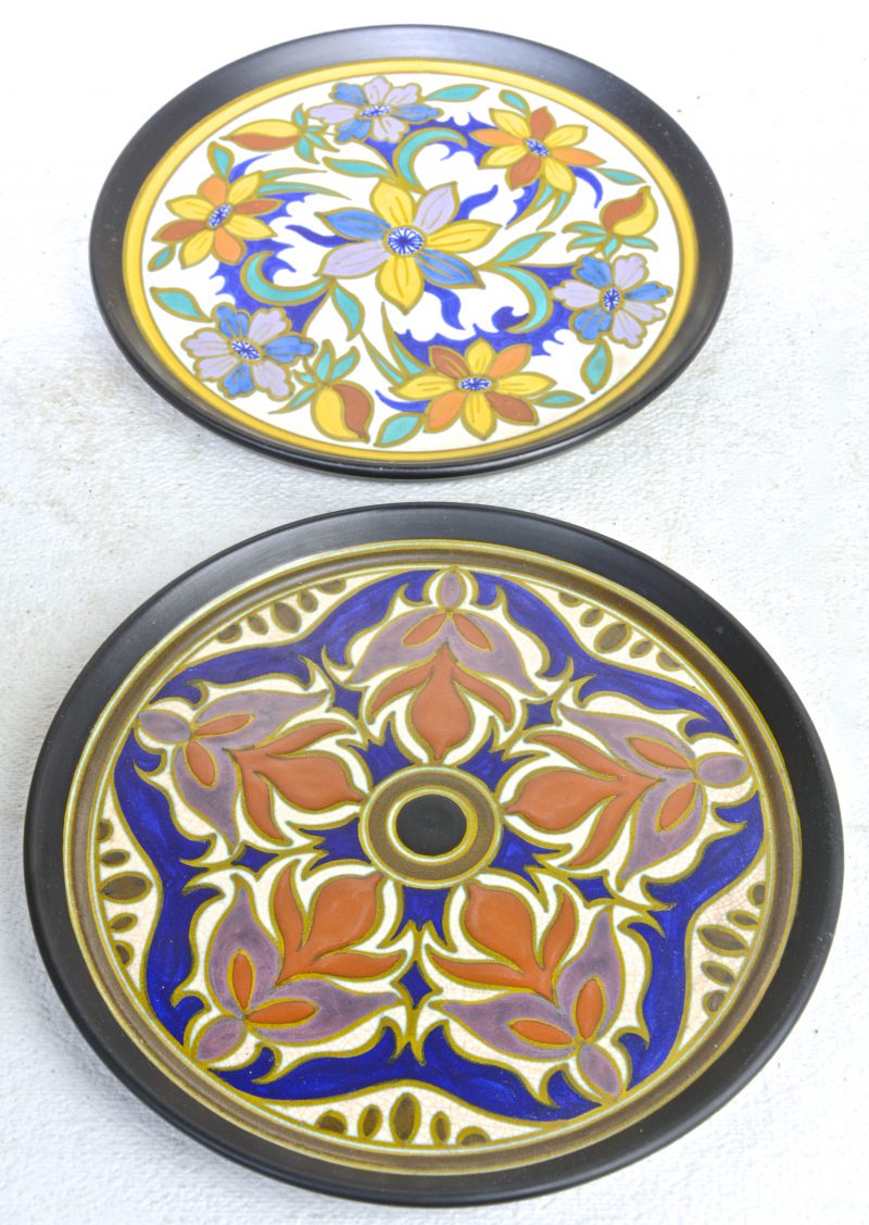 Twee ronde schotels van meerkleurig plateel met decors ‘Ciramat’ & ‘Bacona’. Onderaan gemerkt.