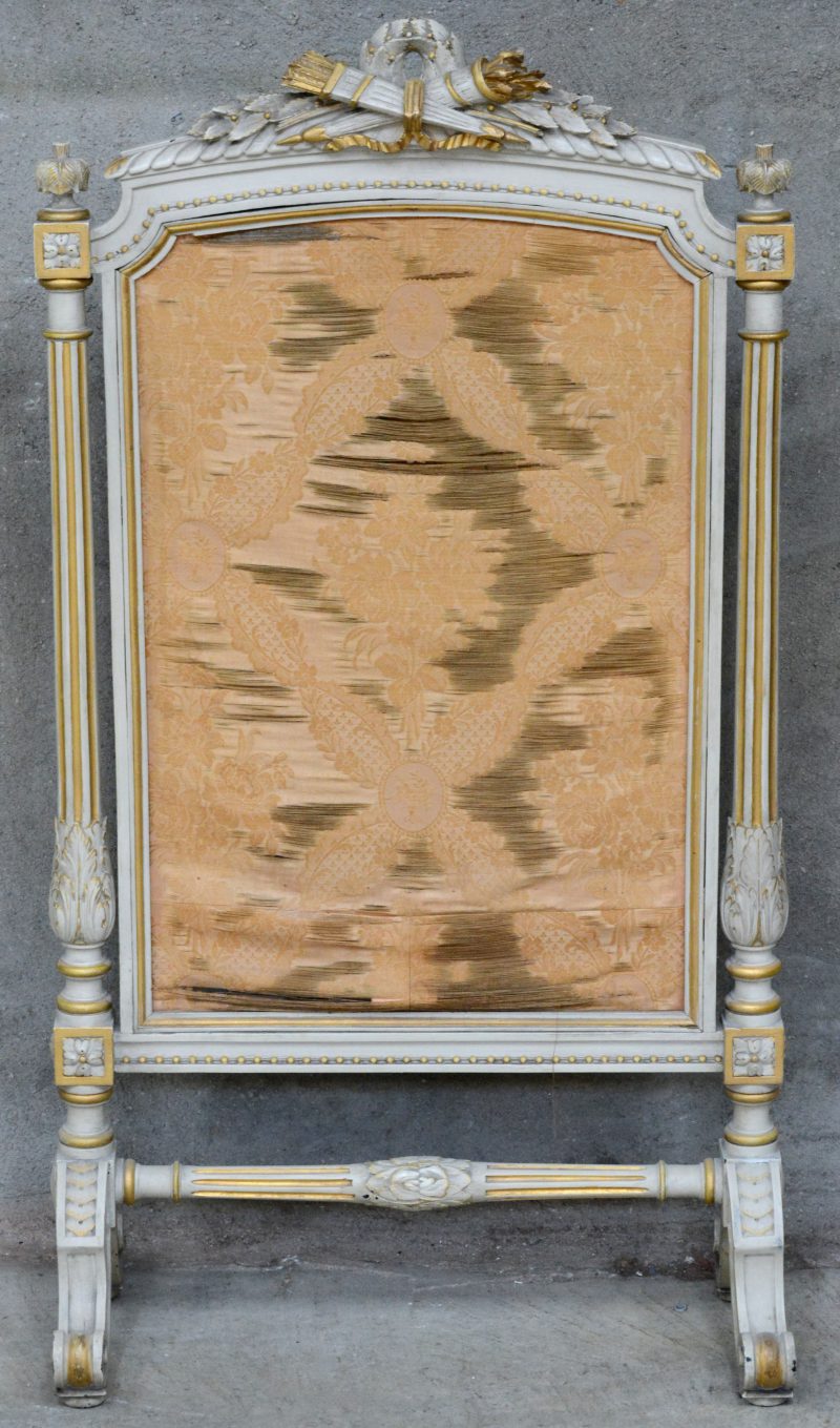 Een gebeeldhouwd en goud en grijsgepatineerd haardscherm in Lodewijk XVI-stijl. Zijde doek sletig.