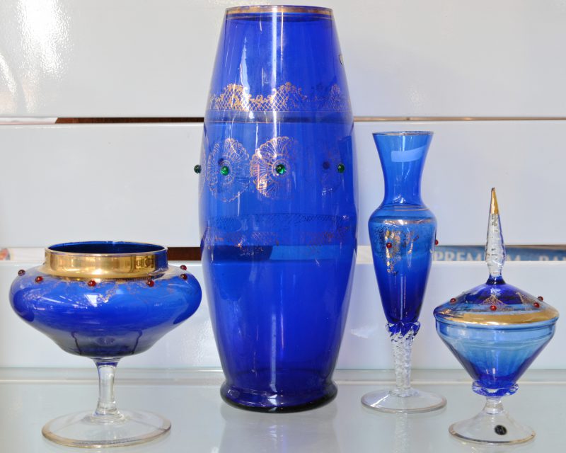Een lot blauw glaswerk met vergulde decors, bestaande uit een drageoir, twee verschillende vazen op voet en een hoge vaas.