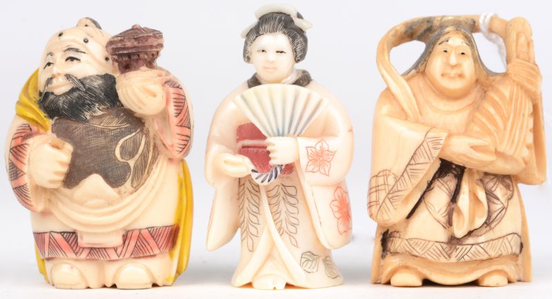 Een geisha en twee andere. Drie netsukes van gebeeldhouwd en deels gekleurd ivoor. Onderaan gemerkt.