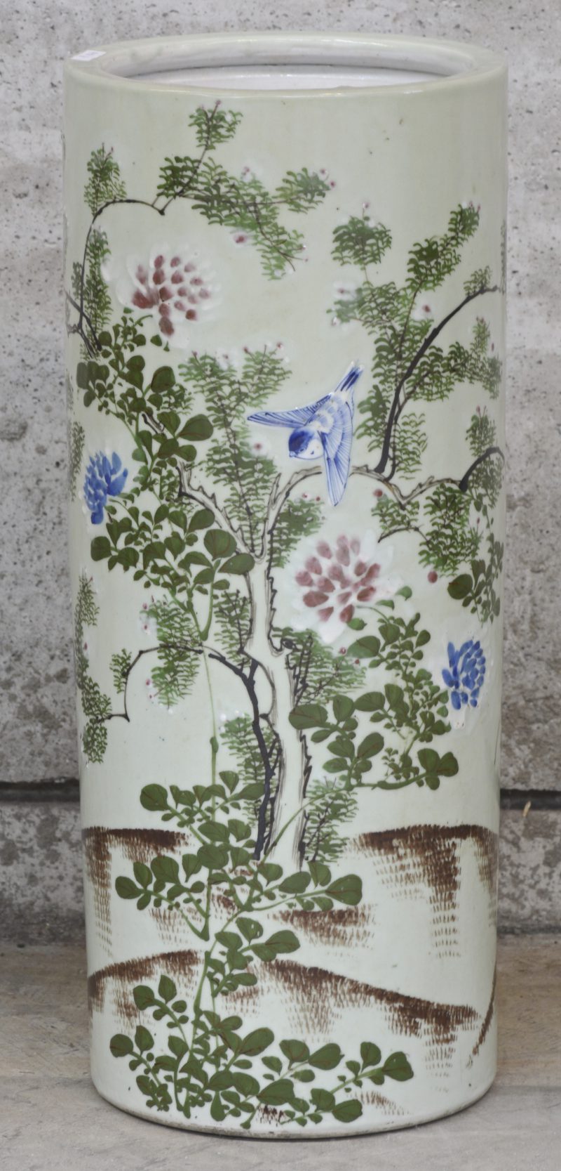 Een cilindervormige paraplubak van celadongroen porselein, versierd met een meerkleurig decor van bloeiende planten en vogels.
