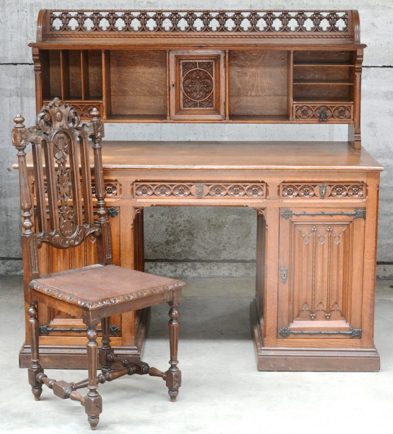 Een gebeeldhouwd eikenhouten bureau met opzet in neogotische stijl. Onderaan drie laden en twee deuren, in het opzet een deurtje en twee laden. We voegen er een gebeeldhouwde stoel in barokke stijl aan toe.