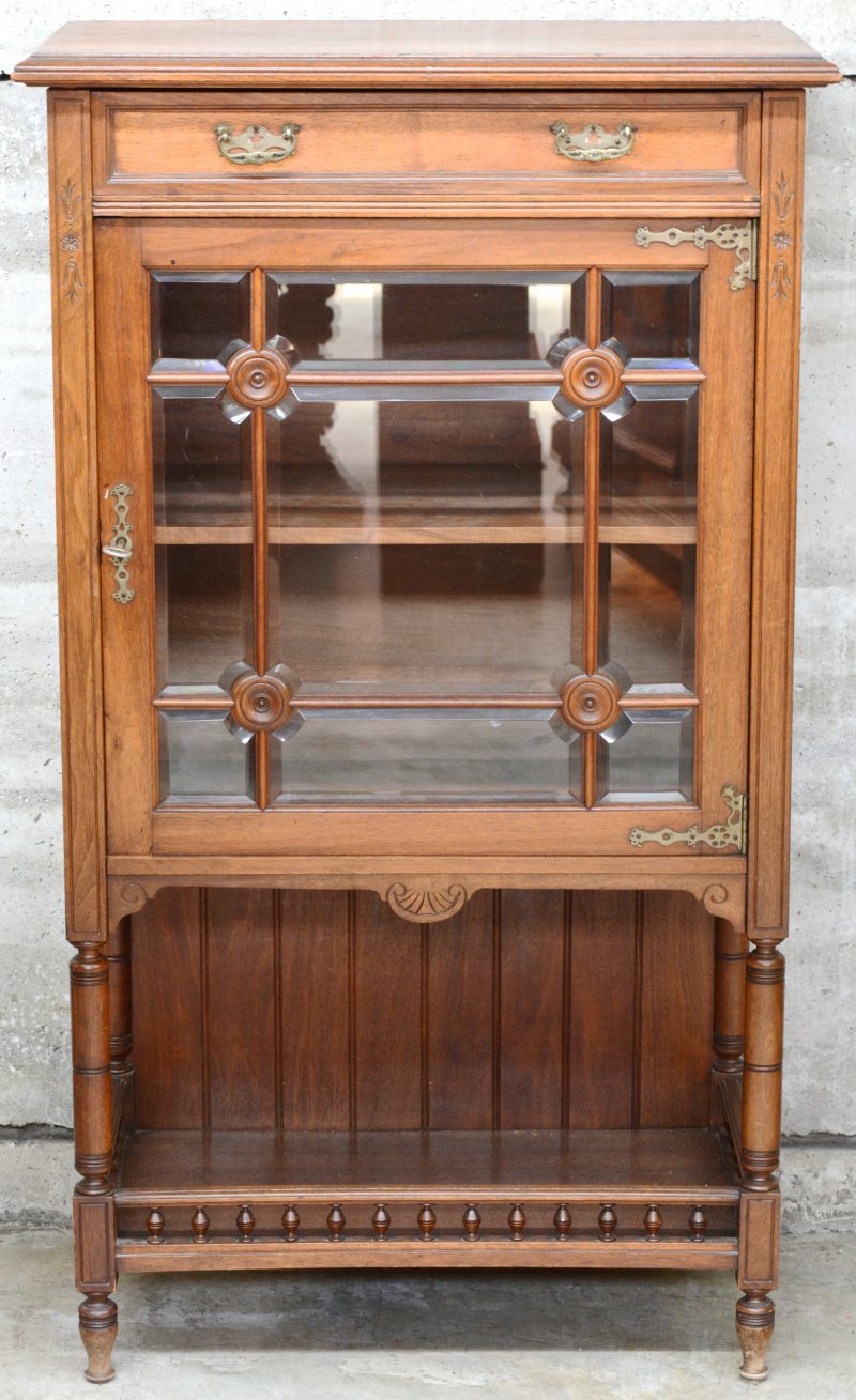 Een kleine vitrine met facetgeslepen glas in de deur en een lade bovenaan.