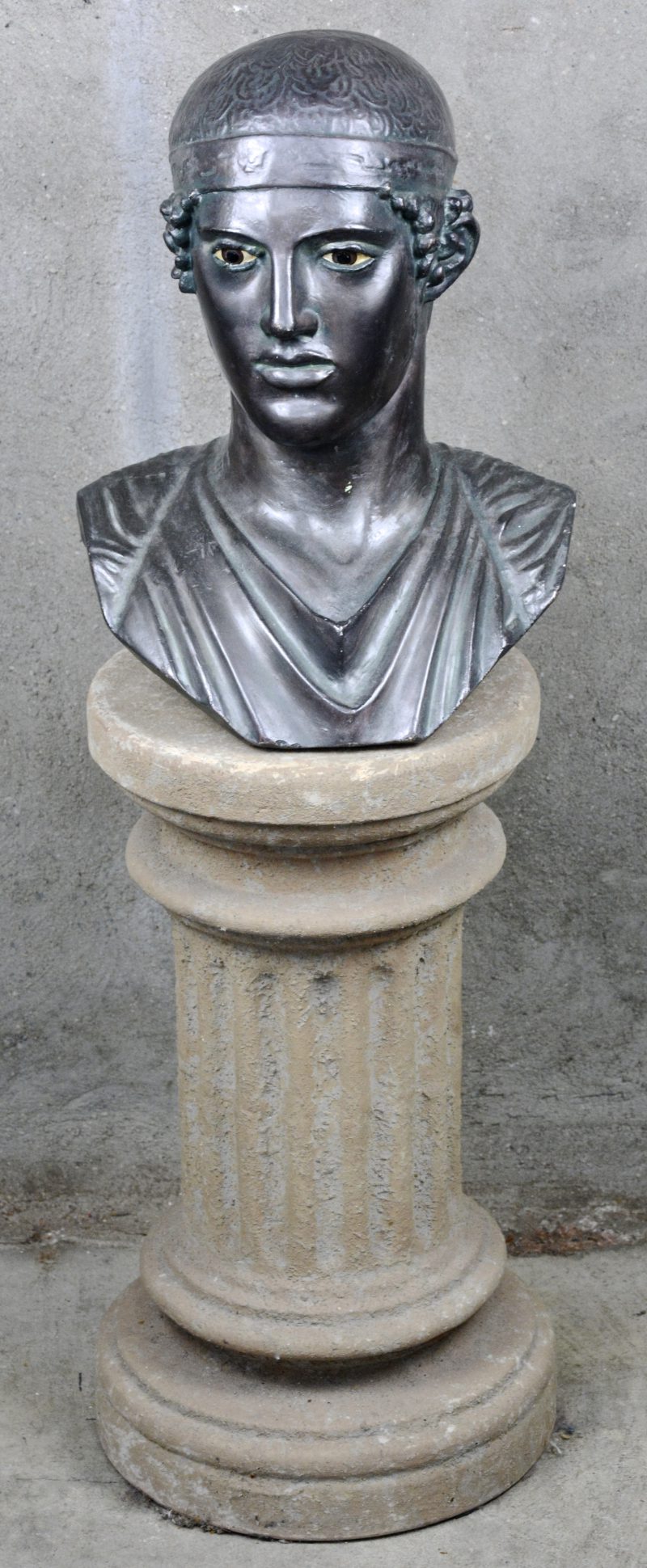 Een gepatineerde plaasteren buste in klassieke stijl op een sober aardewerken zuil.