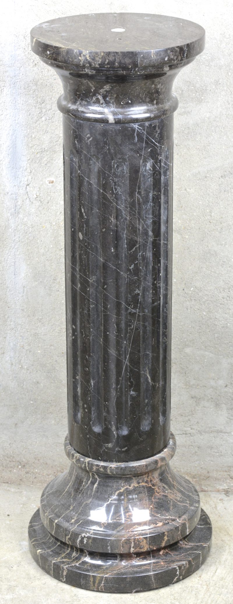 Een zuilvormige piëdestal van zwart marmer.