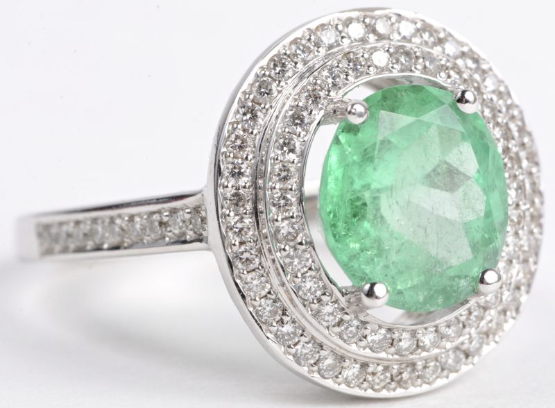 Een 18 karaats wit gouden ring bezet met diamanten met een gezamenlijk gewicht van ± 0,55 ct. en een centrale smaragd van ± 2,20 ct.