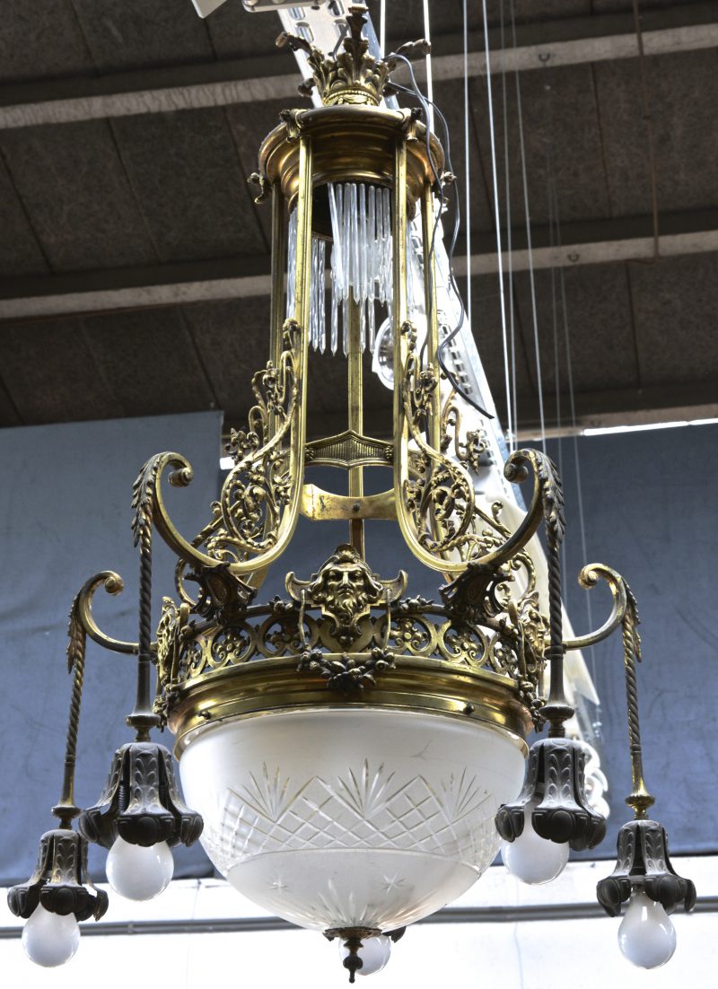 Een messingen luchter met vijf hangende lichtarmen, een gesatineerde en geslepen centrale coupe en bovenaan versierd met glazen pegels. XIXe eeuw.