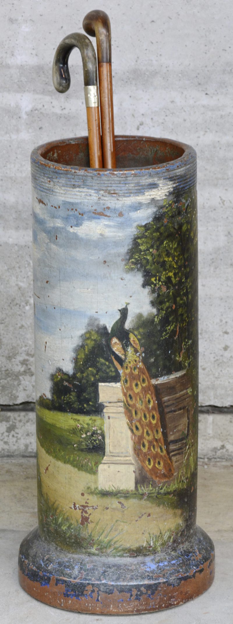Een aardewerken buis, beschilderd met een decor van een pauw in een park en gebruikt als paraplubak. Bijgevoegd vier oude wandelstokken.