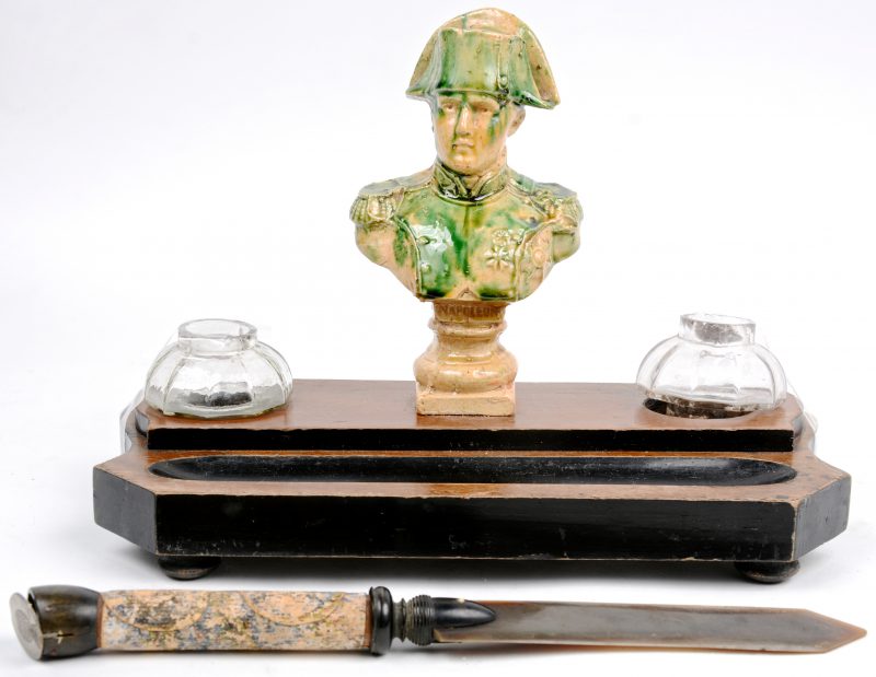 Een houten inktstel met glazen inktpotjes en met een Napoleonbuste van geglazuurd aardewerk. We voegen er een brievenopener aan toe.