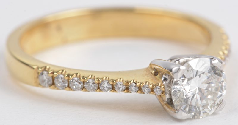 Een 18 karaats wit en geel gouden ring bezet met een centrale diamant van ± 0,75 ct. en diamanten met een gezamenlijk gewicht van ± 0,30 ct.