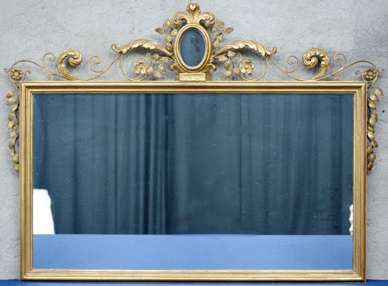 Een rechthoekige vergulde spiegel  met barokke versieringen bovenaan.