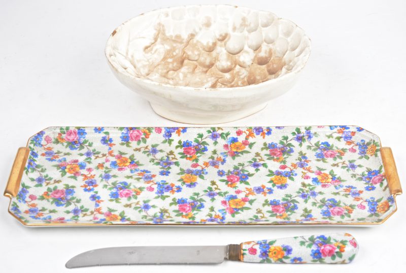Een cakeschaal van meerkleurig en verguld porselein met bijpassend mes, versierd met een bloemendecor. We voegen er een aardewerken pudding-/cakevorm aan toe.