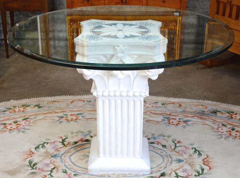 Een tafel met rond glazen blad op een voet van witgepatineerd composiet in de vorm van een Corinthische zuil.