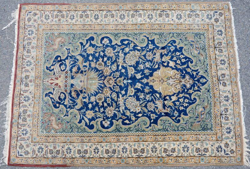 Een handgeknoopt Perzisch karpet met een decor van dieren en bloemen.