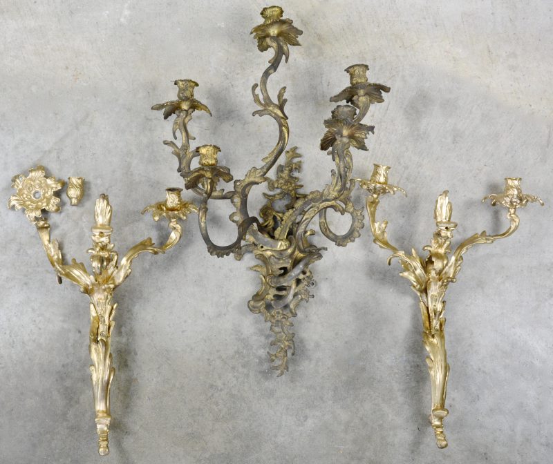 Een paar bronzen wandkandelaars in Lodewijk XV-stijl. We voegen er een derde, afwijkend exemplaar aan toe.