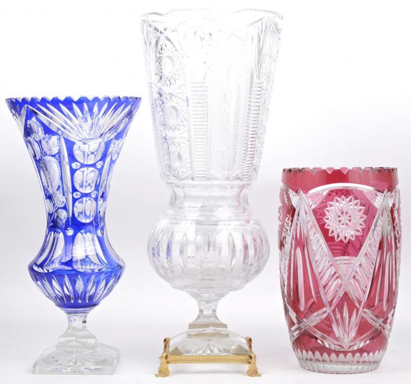 Een lot geslepen Boheems kristal, bestaande uit een rode vaas, een blauwe vaas p voet en een kleuloze op voet met messingen montuur.
