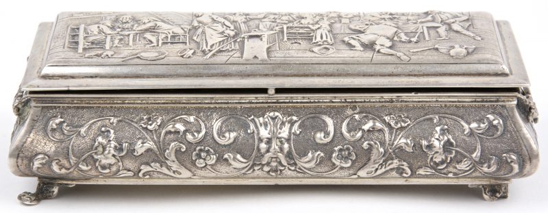 Een gedreven zilveren doos met barokke versiering. Op het deksel een scène naar David Teniers in reliëf. Hollandse keuren, tweede gehalte. Makersmerk EMB. Letsels aan twee pootjes.