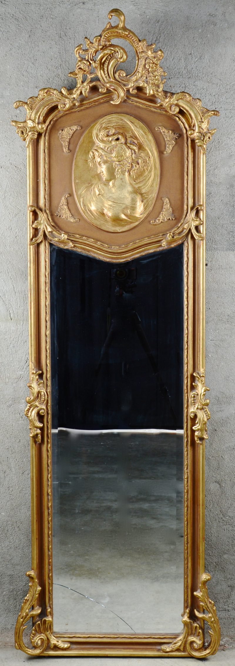 Een verguld houten spiegel in Lodewijk XV-stijl, versierd met een bas-reliëf met een jonge vrouw in profiel. Glas gebarsten.