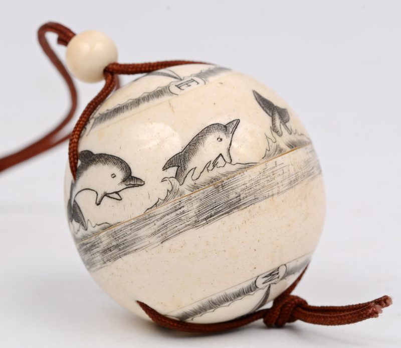 Een benen bol met gegraveerd decor van zeilschepen en dolfijnen.