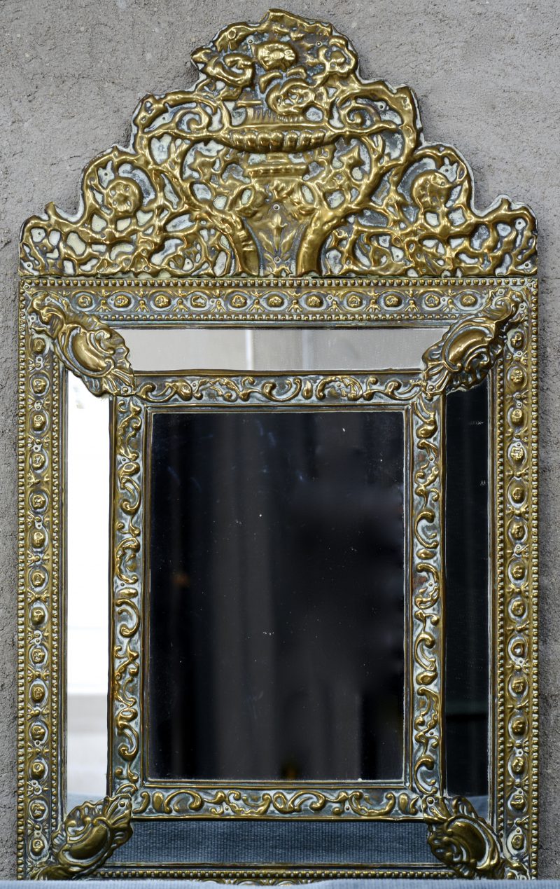 Een spiegel met lijst van gedreven messing in barokke stijl.