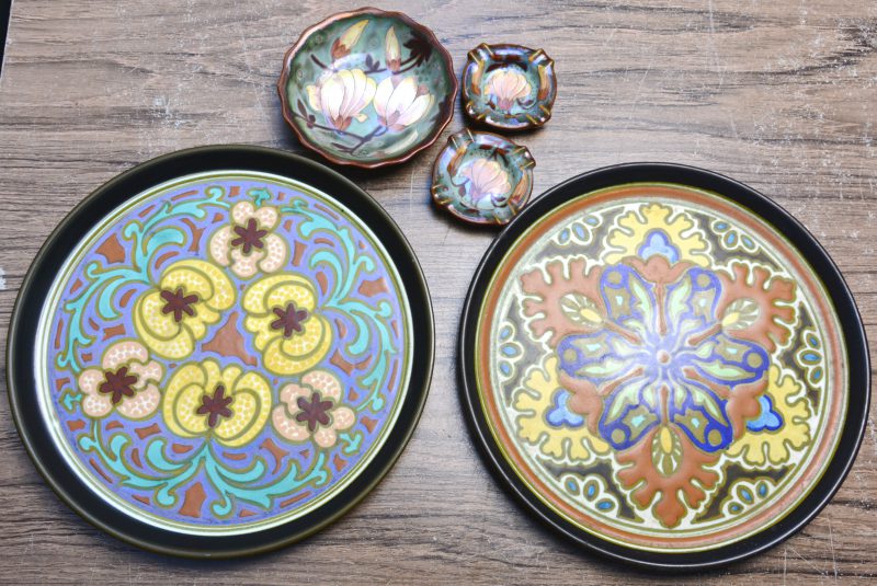Twee ronde schotels van meerkleurig aardewerk en een schaaltje en twee asbakjes met decor ‘Unique metalique’. Alen gemerkt.