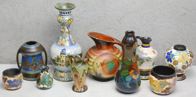 Een lot meerkleurig Gouda-aardewerk, bestaande uit een glanzende vaas met bloemendecor, een oorvaas (kleine schilfer), een kruikje, een vaas, een kleinvaasje, een knubbelvaas, twee potjes en twee schenkkannen.
