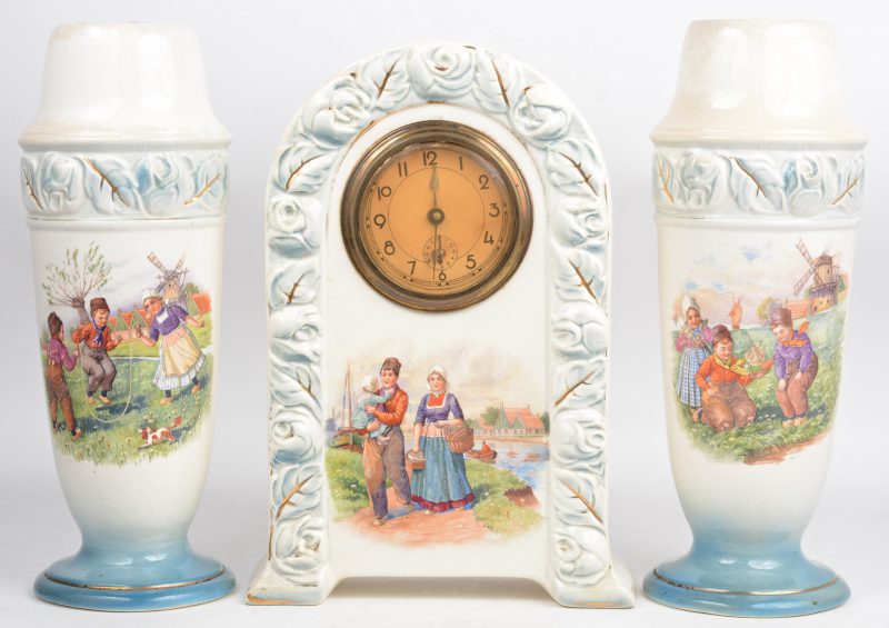Een driedelig schouwstel van meerkleurig aardewerk, bestaande uit een pendule en twee vazen, gedecoreerd met een Hollands gezin.