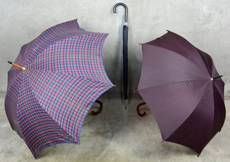 Twee verschillende paraplu’s met houten handvat en één met lederen handvat.