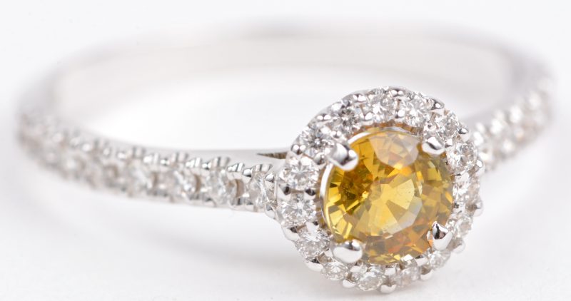 Een 18 karaats wit gouden ring bezet met diamanten met een gezamenlijk gewicht van ± 0,25 ct. en een gele saffier van ± 0,50 ct.