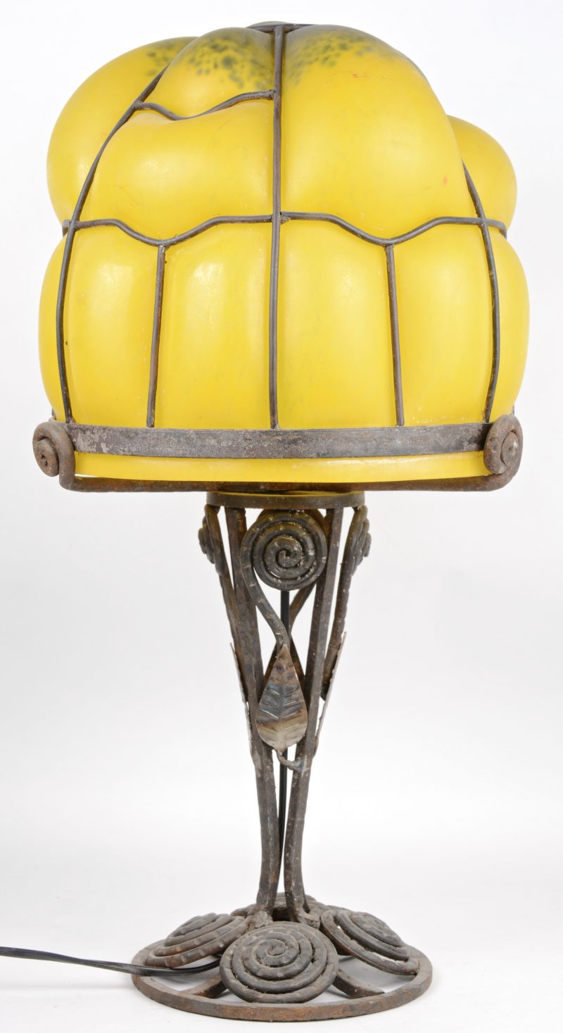 Een smeedijzeren lampenvoet met een geel glazen kap. Begin XXe eeuw.