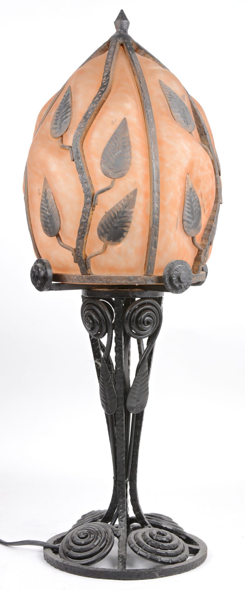 Een smeedijzeren lampenvoet met oranje glazen kap, versierd met smeedijzeren blaadjes. Begin XXe eeuw.