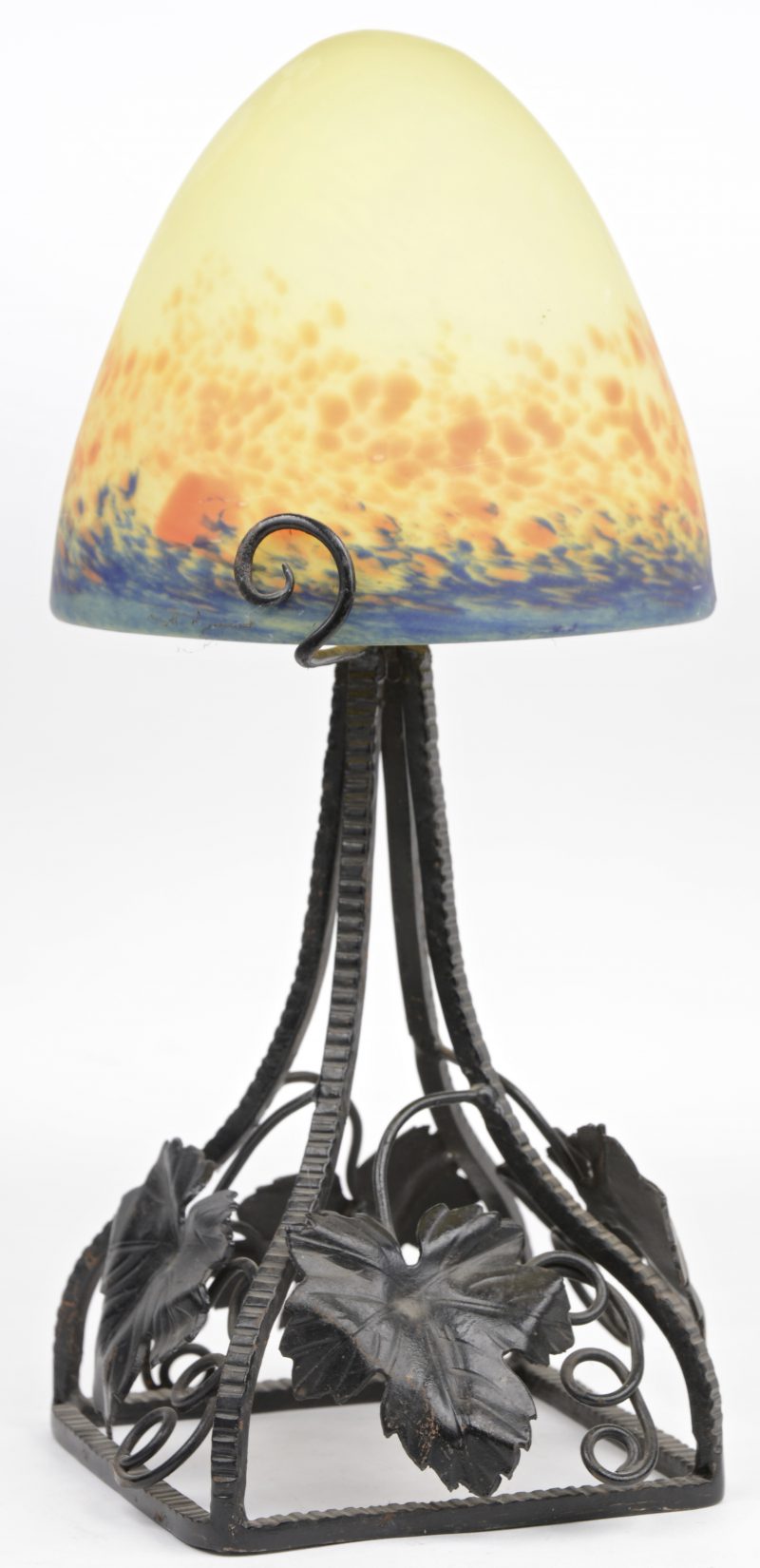 Een smeedijzeren lampenvoet, versierd met druivenbladeren en met een kap van meerkleurig glaspasta. Begin XXe eeuw.