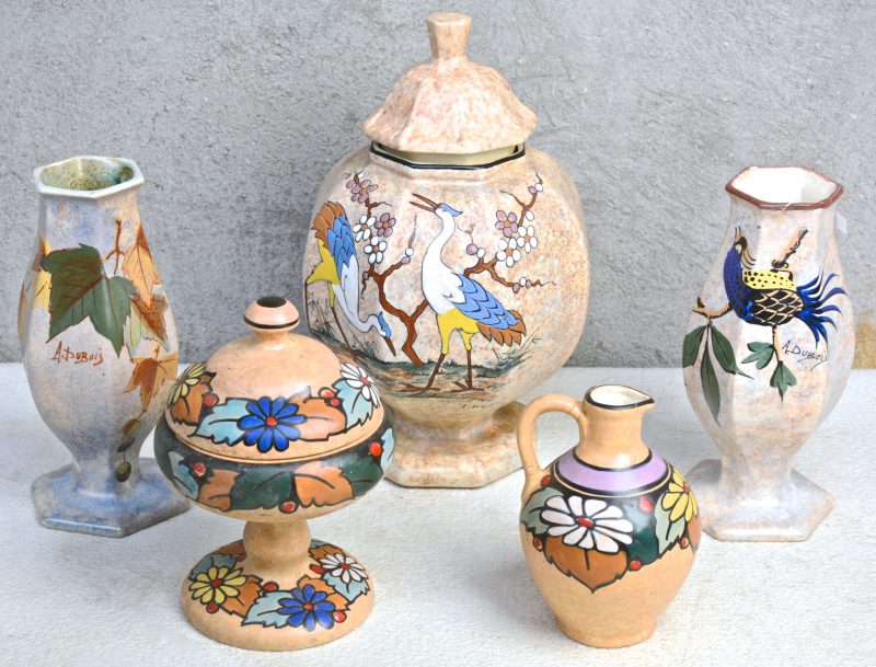 Een lot meerkleurig aardewerk, bestaande uit een bonbonnière op voet, een kruikje (restauraties), twee zeshoekige vazen (één gerestaureerd) en een dekselvaas, versierd met decors van A. Dubois.