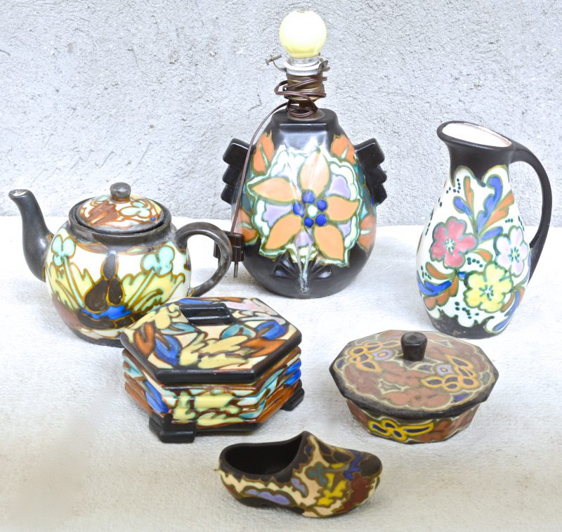 Een lot meerkleurig aardewerk in de stijl van Gouda, bestaande uit een theepot, twee dekseldozen, een lampvoet, een klompje en een kan. Gemerkt.