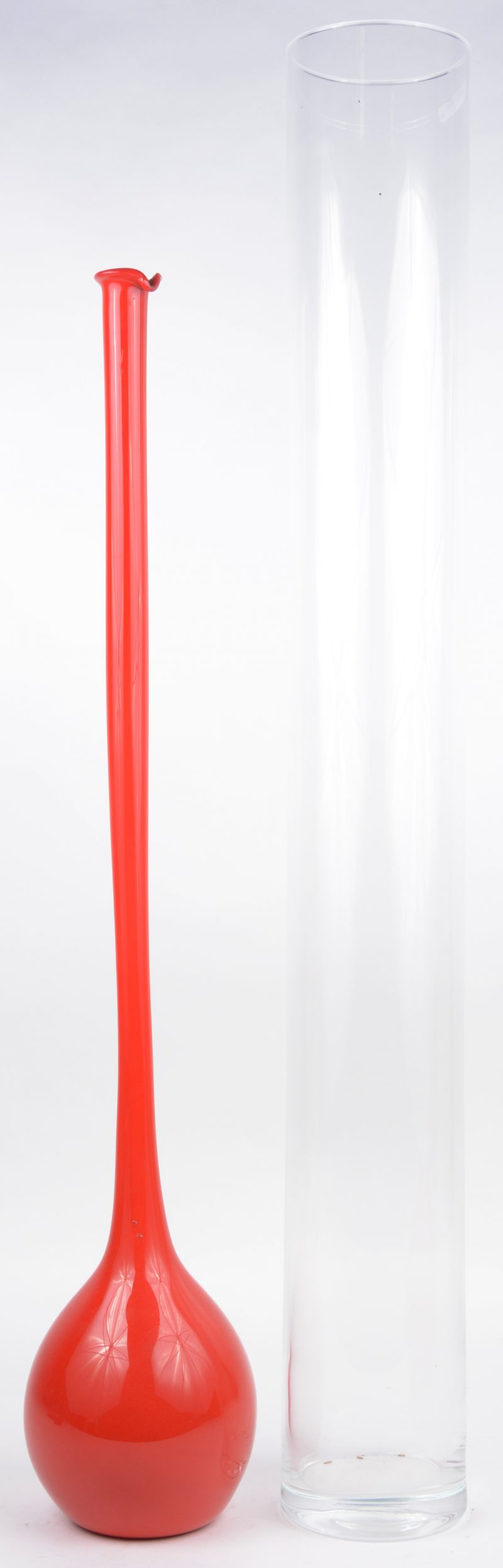 Een lange kleurloos glazen cilindervaas en een rode bolle vaas met lange hals.