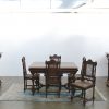 Eikenhouten eetkamer in Henri II-stijl, bestaande uit twee tweeledige buffetten met telkens onderaan twee paneeldeuren en bovenaan een spiegeldeur, een tafel met parketwerk en zes stoelen met gecanneerde zit en rug.