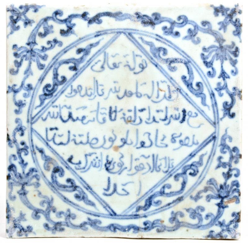 Een porseleinen tegel met Arabische geschriften en motieven in blauw op witte fond.
