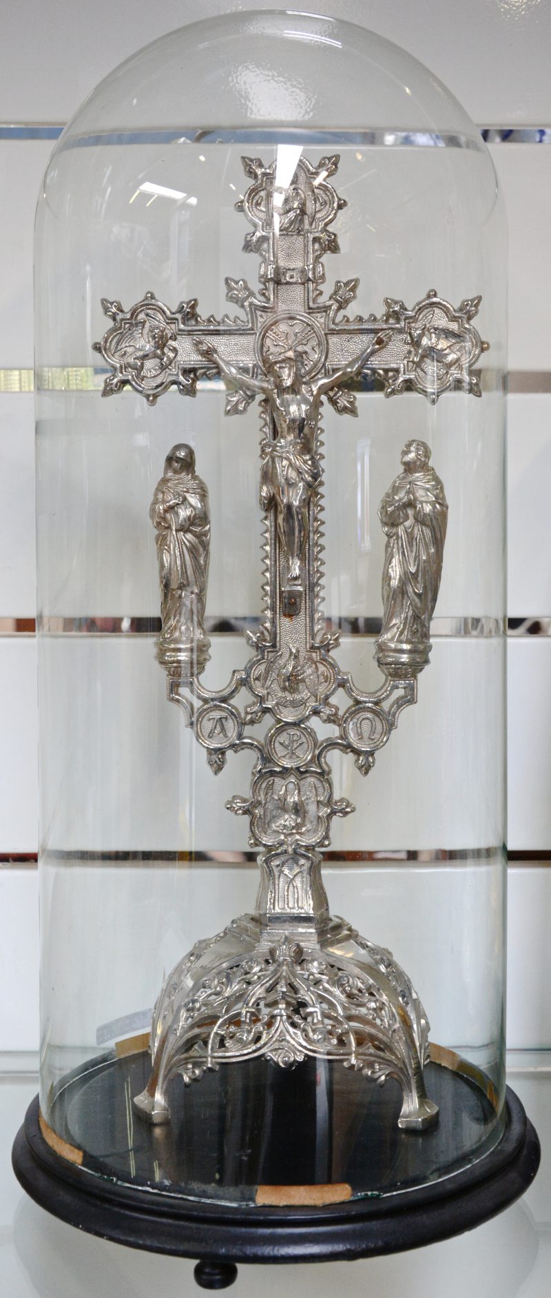 Een verzilverd metalen kruisbeeld onder glazen stolp.