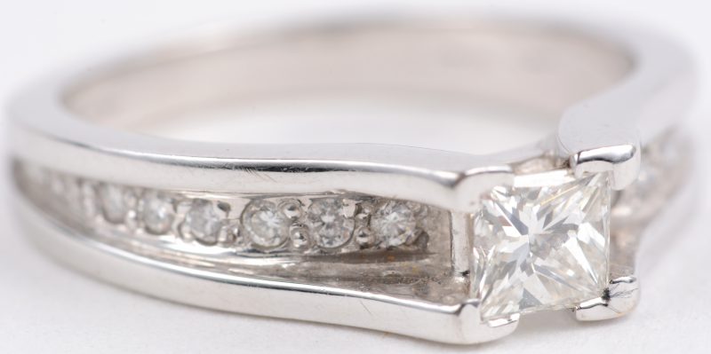 Een 18 karaats wit gouden ring bezet met briljanten met een gezamenlijk gewicht van ± 0,15 ct. en een diamant in princess cut van ± 0,50 ct.