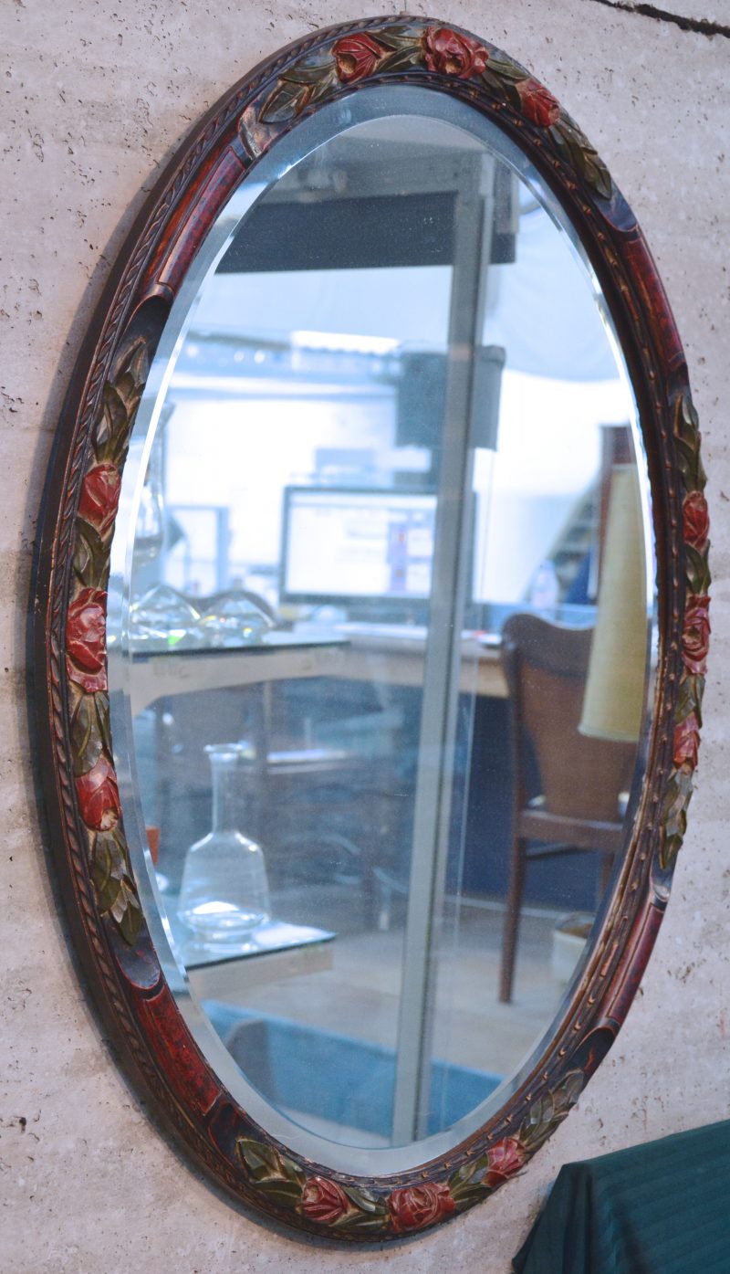 Een ovale spiegel met gebeeldhouwde en gepolychromeerde houten lijst.